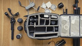 Professional  photographer packs smart backpack with equipment, holding lens. Top view on suitcase with lens,camera, drone and gimbal