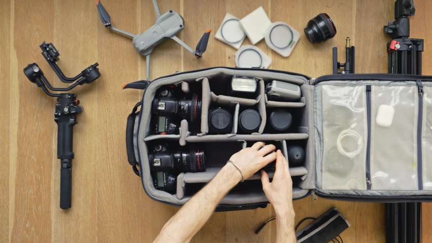 Professional  photographer packs smart backpack with equipment, holding lens. Top view on suitcase with lens,camera, drone and gimbal