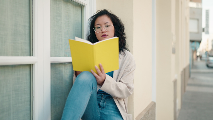 Young chinese woman reading book at street