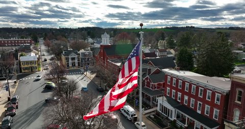 American flag waves in slow motion in USA small town. Bright sunny day with beautiful sky. Aerial establishing shot.