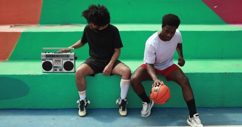 Young african people listening music from vintage boombox stereo outdoor after basketball match