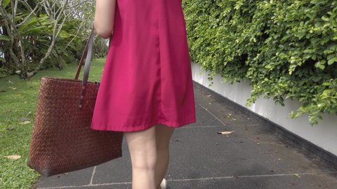 An asian young woman wear red dress carrying beach tote bag walking on pathwat to the beach paradise in summer vacation in slowmotion
