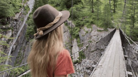 Follow me to, woman holding companion's hand, leading him on a hike over suspension bridge in the forest 