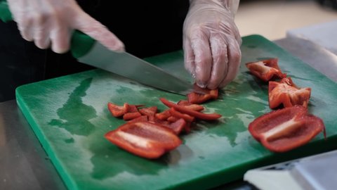 Close up shot of chef's hands cutting a fresh red bell pepper with knife on wooden board. Cooker preparing vegetarian salad in kitchen, 4k footage
