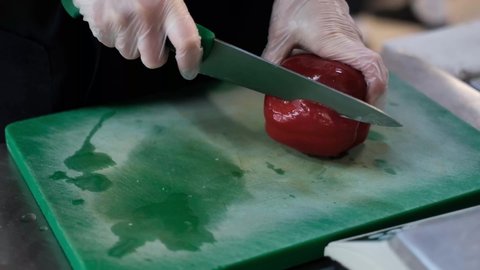 Close up shot of chef's hands cutting a fresh red bell pepper with knife on wooden board. Cooker preparing vegetarian salad in kitchen, 4k footage