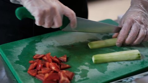 Female cook cuts vegetables, prepares a delicious fresh salad for lunch, cuts a cucumber on a green board with a green knife