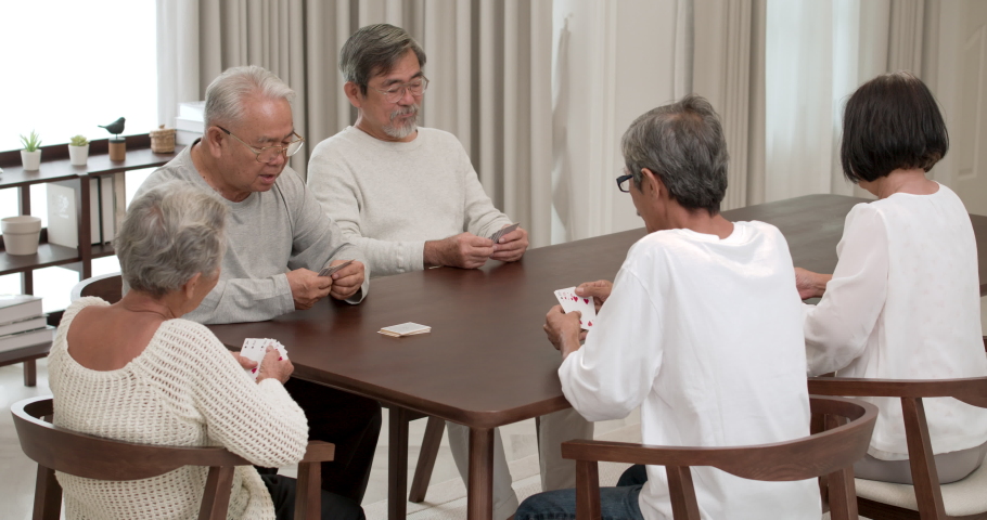 A Group of happy Asian seniors male and female sitting and having fun by playing cards with a smile in cozy common room at nursing home. Elderly men and women spending free evening together indoors. Royalty-Free Stock Footage #1089435563