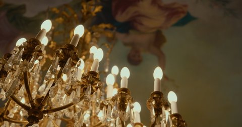 Golden chandelier with a baroque style crystal pendants, hung behind a renaissance oil painting. Light and gilding, wedding at the town hall in an old room.