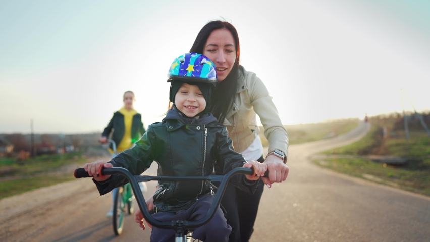 Childhood bike concept. Mother teaching son to ride bicycle. Young mom teaching son to ride bike first time on countryside rural road at sunset. Happy kids on bikes. The best moments together. Royalty-Free Stock Footage #1089436391