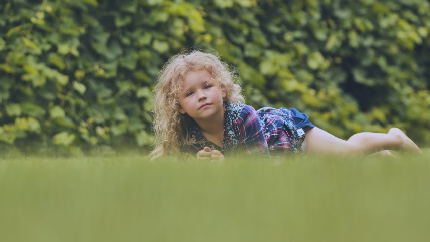 A little curly-haired girl lies on the grass in the garden.