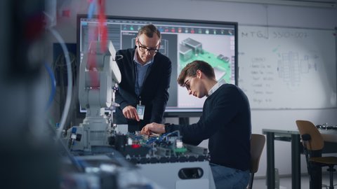 Male Student Engineer Discussing Ideas with Project Leader while Working with Computer Motherboard. Man Uses Screwdriver. Science, Robotics and Engineering Concept. Medium Shot