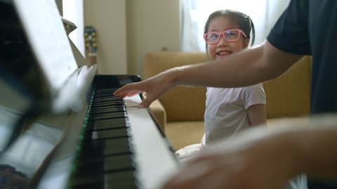 Scene of young kid sitting on the bench looking up happily enthusiastic learning piano while the teacher teaching and introducing her to playing new songs, early childhood education, music education.
