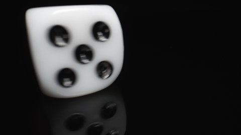A White Game Dice Spinning on One Spot on a Black Table and a Black Background. Chance Options. Devil's Bones
