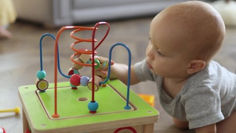 little toddler baby child playing toys on floor home, abacus developing, learning to take and touch things, trying to stand and reach colorful toys. child baby exploring world around him indoors.