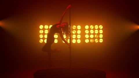 Pole dancer lady making beautiful trick on pylon indoors. Attractive woman moving body sexually spinning on stage spotlights. Hot sporty girl performing erotic poledance in nightclub backlight. 