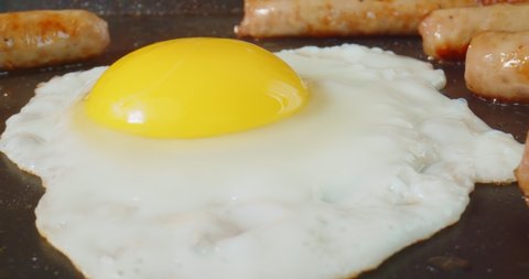 Macro probe footage of breakfast sausage and eggs being cooked on a griddle. 4K slider shot.