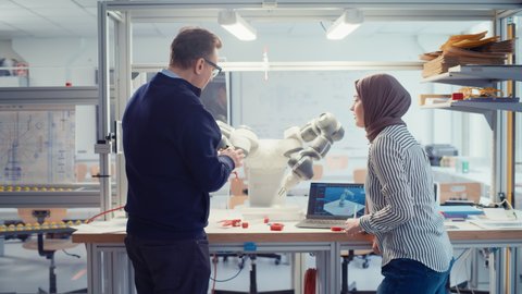 Chief Male Engineer Chatting with Arabic Female Computer Science Specialist While Gathering at the Table with Robotic Hand. Promising Computer Scientist Collaboration Concept. Medium Shot