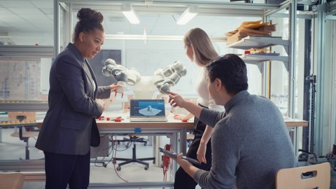 Diverse Group of Computer Science Specialists, Robotics Engineers Work on  Autonomous Manufacturing Facility concepts with Black Senior Engineer. Developing Software for Robotic Arm control