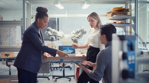 Chief Female Engineer Collaborates on Robot Arm Development with a Group of Young Specialists, Scientists, Visioners. Professionals Work on Autonomous Facility Research, Use Programmable Robot Hand