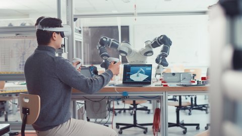 Student Male Engineer Wearing AR Headset Designs and Manipulate Robot Hand while Using Controllers. Futuristic Virtual Design of Mixed Technology Application Concept