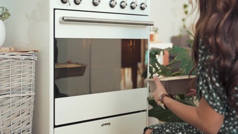 Slow motion shot of a woman dressed in a green dress placing a cake into a white oven