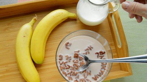 HD video, chocolate cornflakes in the form of an alphabet with milk in a bowl. Top view of a breakfast tray with bananas, pouring milk from a jug.