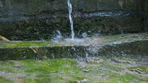 Beautiful small fountain in a slow motion. Rocks, stones and green moss. Water splashes. Horizontal video.