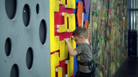 Child boy training active on climbing wall. Children's rock climbing in a private school. Climbing exercises. School-age girl climbs the wall of a climbing wall.