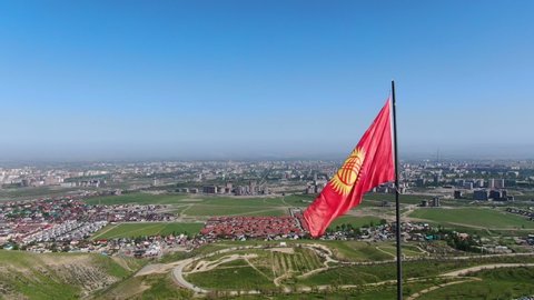 Aerial view of Bishkek city from the mountains. Flagpole with waving Kyrgyzstan flag