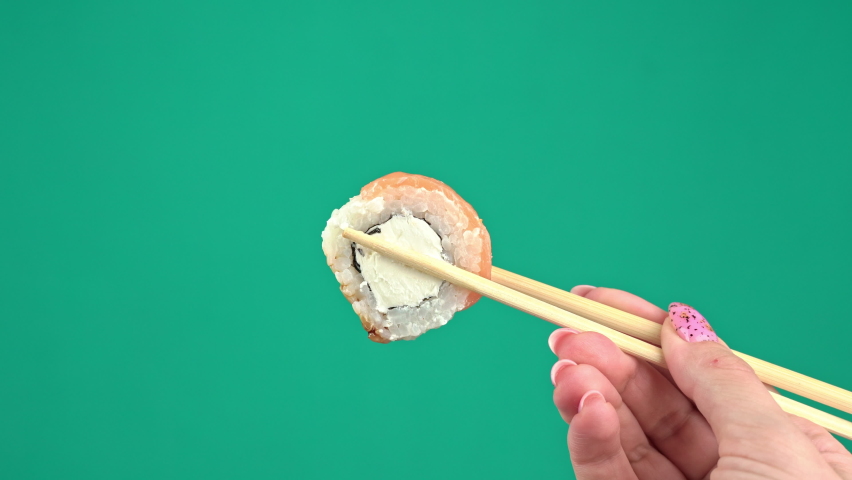 Female hands hold Japanese chopsticks with sushi rolls on green background. Alpha channel hand with chopsticks sushi close up. Japanese cuisine, fish dishes. Chroma key for background replacement. | Shutterstock HD Video #1089456415