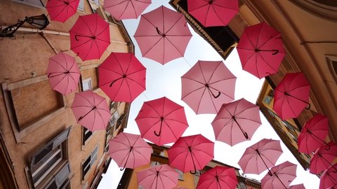 Grasse, France, October 3, 2021: TIMEWARP Suspended pink umbrellas in the historic center of Grasse, celebrating the Rose Expo. Elements of architecture of Grasse with colored umbrellas between houses