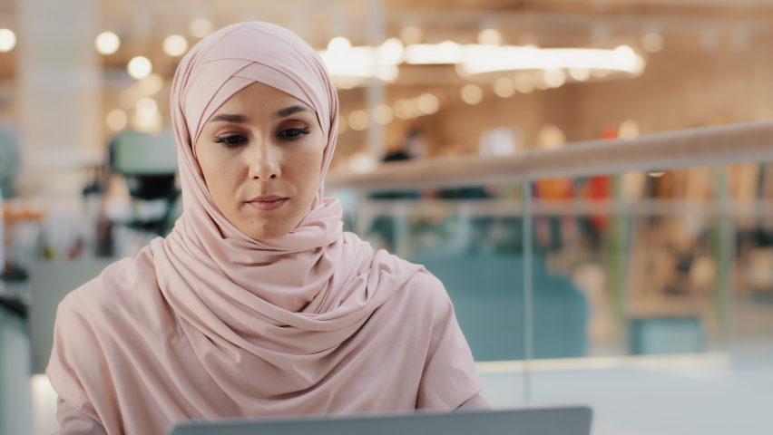Young pensive puzzled arab woman in hijab working on laptop concentrating on idea looking for inspiration keeps hand on chin thinking deeply in thoughts looking for solution to problem finds answer Royalty-Free Stock Footage #1089458613