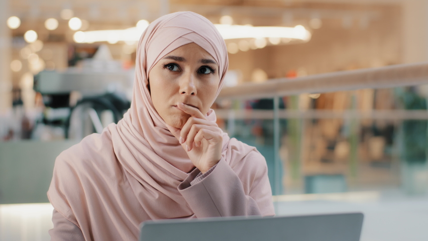 Young pensive puzzled arab woman in hijab working on laptop concentrating on idea looking for inspiration keeps hand on chin thinking deeply in thoughts looking for solution to problem finds answer Royalty-Free Stock Footage #1089458613