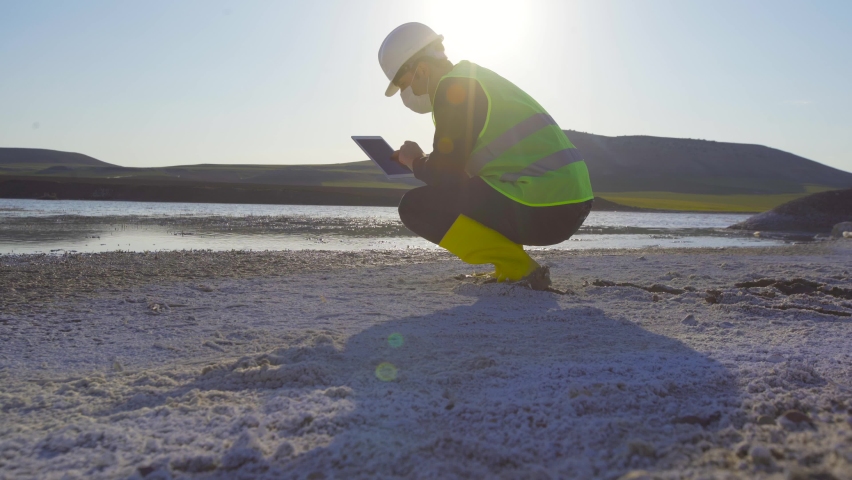 Environment and water pollution, engineer working.
Analyzing the chemical pollution in the lake, the engineer is working on the tablet. There is white chemical waste by the lake.