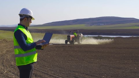 Tractor agrochemical and engineer.
Agricultural spraying is done by the tractor on the soil agricultural land. An engineer is working on the laptop in his hand.