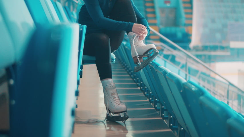 Female skater is lacing up her skates on the bleachers