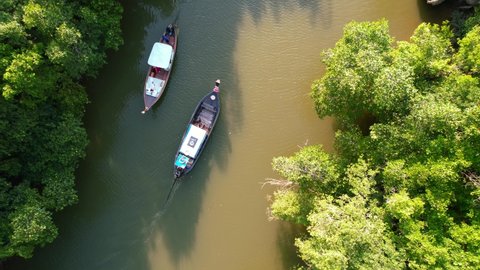 top down aerial drone of two wooden Thai longtail boats pass each other on the river surrounded by mangrove forests in Krabi Town Thailand during a sunset afternoon