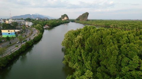 aerial drone flying low over an island forest surrounded by a river and limestone mountains (Khao Khanap Nam) as cars pass on a highway road during golden hour sunset in Krabi Town Thailand