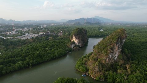 Aerial drone panning left over a river running between two large limestone mountain rocks (Khao Khanap Nam) on a sunset afternoon in Krabi Town Thailand