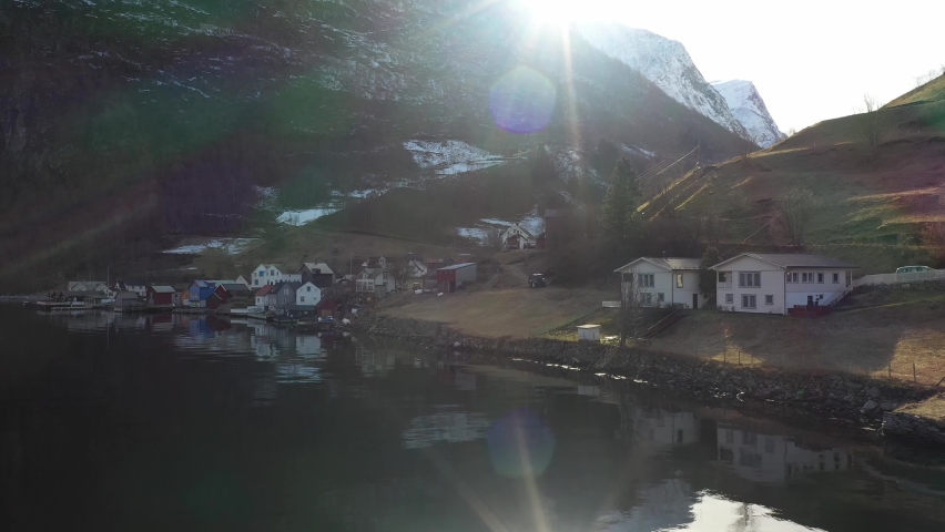 Low altitude aerial presenting town of Undredal during early morning sunrise - Seen from seaside with sun above mountain peak and mountain valley background