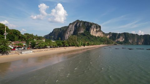 aerial drone flying up looking over Ao Nang Beach and large limestone mountain cliffs in the distance in Krabi Thailand during a sunny summer day