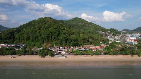 aerial drone flying parallel to Ao Nang Beach in Krabi Thailand revealing buildings and a large mountain hill in the distance on a sunny day