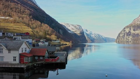 Beautiful early morning in Undredal village close by the majestic Aurlandsfjord in Norway - Low altitude sunrise aerial close to sea passing boathouse