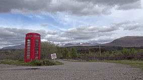 Traditional british phone box in the Highlands with snow on the mountains time lapse