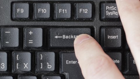 A male finger presses the backspace key on a computer keyboard once and holds it, macro
