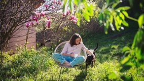 A young beautiful woman enjoying her morning coffee while sitting in a chair in the garden under the magnolia tree and her dog is walking around. - Powered by Shutterstock - Get 15% off with code: PIKWIZARD15