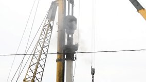 Close-up view of pile driver hammering concrete pile at a construction site. Overcast sky. Slow motion video. Deep foundation theme.