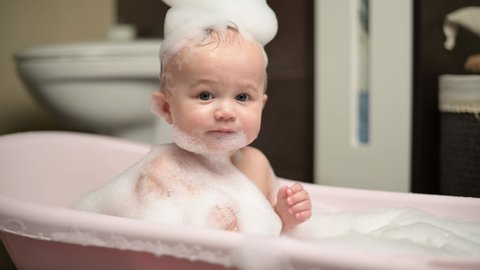 A small child enjoys a bath, splashes in it
