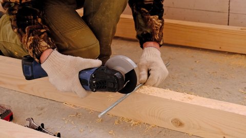 A builder's hands in work gloves cut a metal hairpin with an angle grinder electric tool. Preparation of a log for a wooden floor. Home repair with your own hands, a sawmill. Slow motion