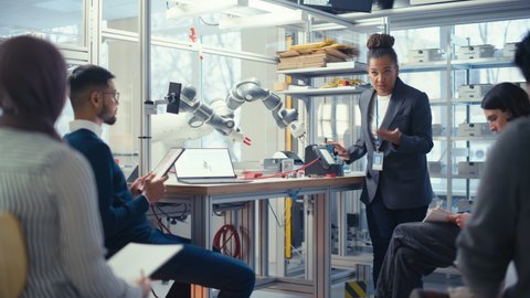 Black Specialist Explain to Diverse Computer Science Specialists While Robot Limb Moving Under her Controlling. People Designing Automated Robotic Systems Concept